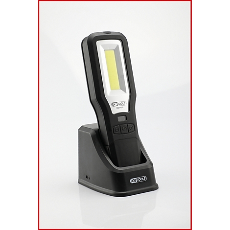 Zwarte werkplaatslamp in laadstation. De kop heeft een rechthoekig, helder LED-gebied.